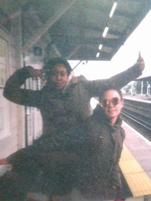 An old picture of Laura and Lovissa at the train station taken on a disposable camera. They are posing, Laura is pouting.