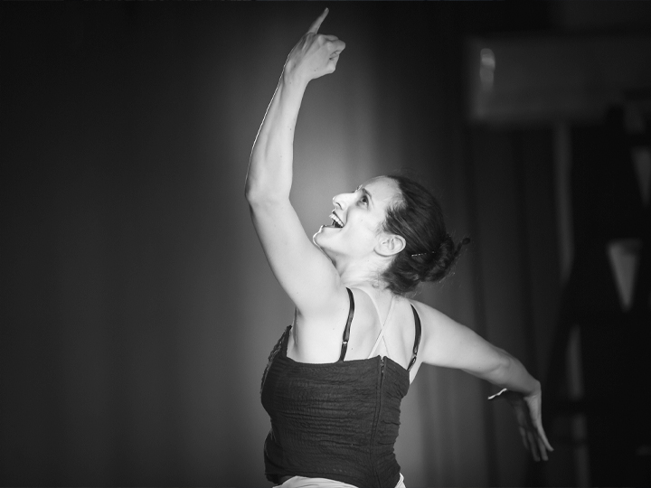 Tal Levy Cohen standing in a ballet position, left arm up, right arm outstretched, looking up to her left