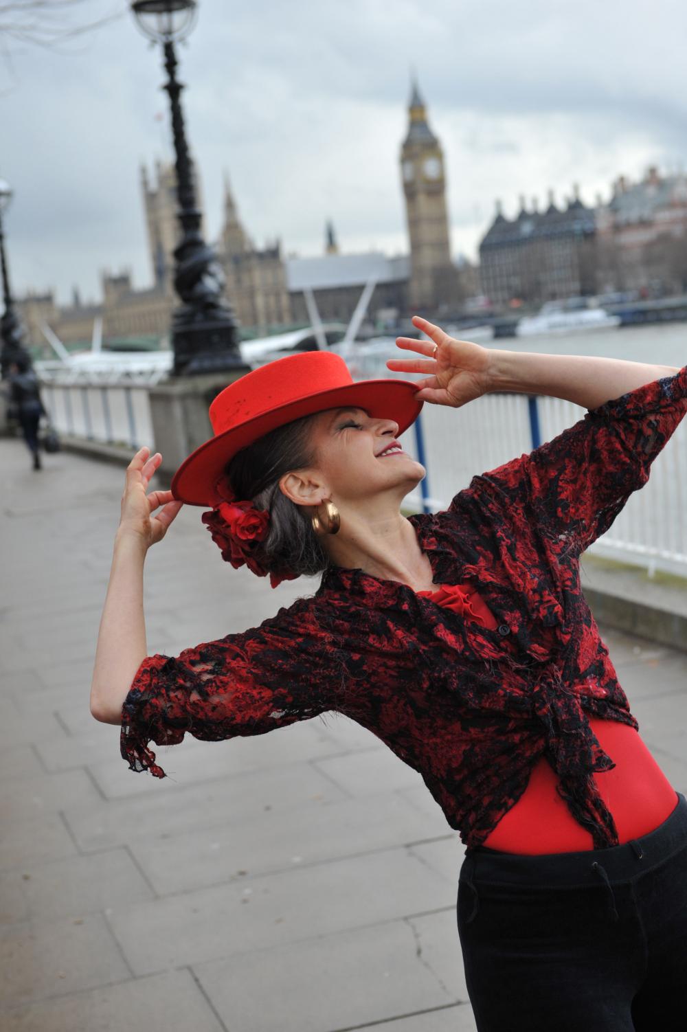 Danielle, of Flamenco Con Gusto, poses in a bright red flamenco hat, on the Southbank, with Big Ben in the background