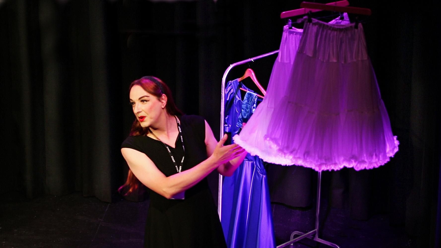 A woman with long red/brown hair, wearing a black dress displays a purple lit retro petticoat hanging from the ceiling.