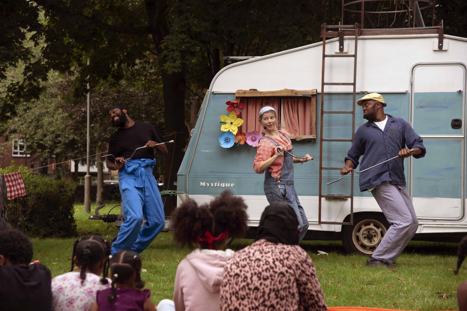 Three people are dancing in front of their caravan.