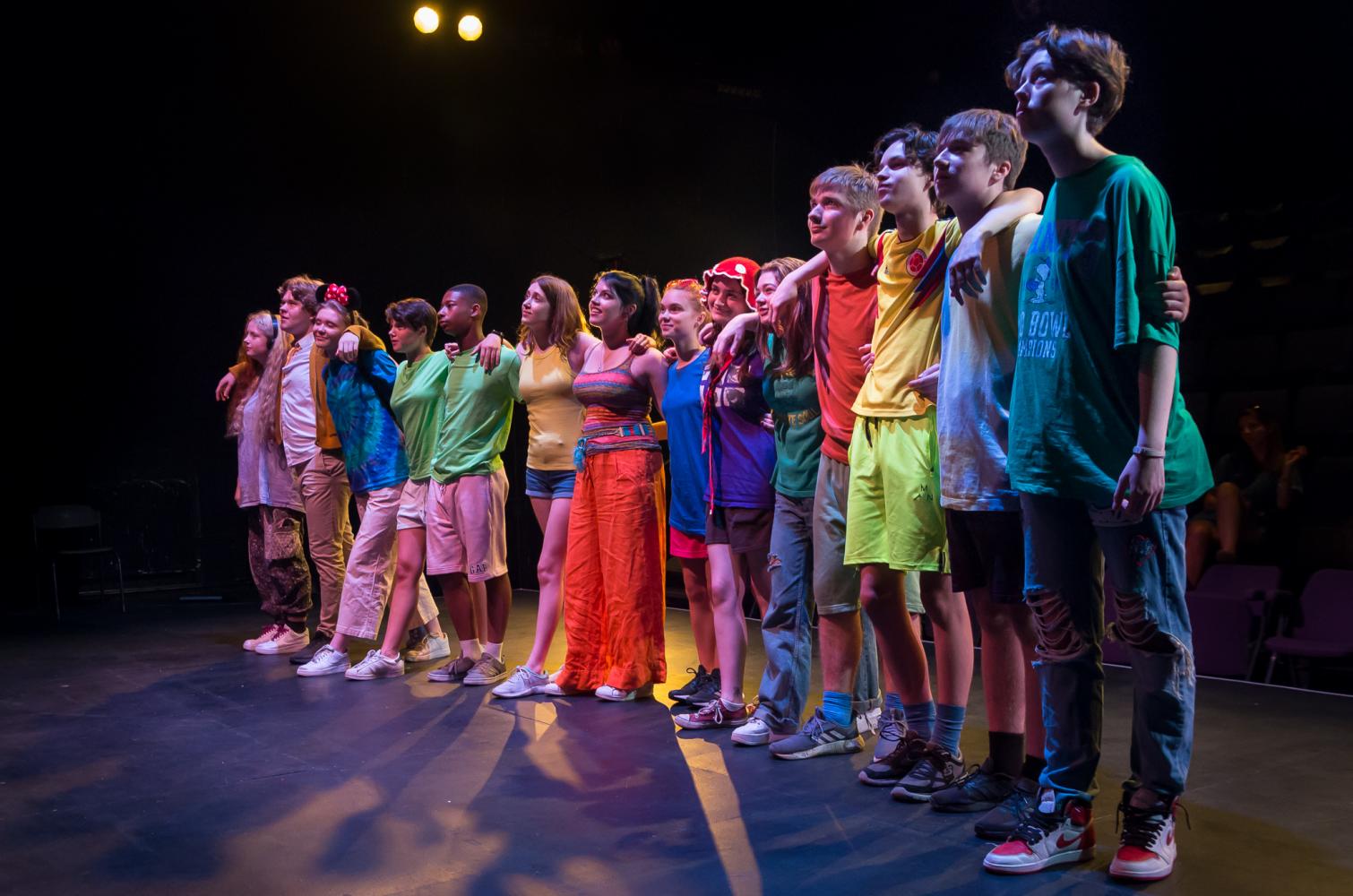 A group of young people stand in a line in colourful clothes looking up.