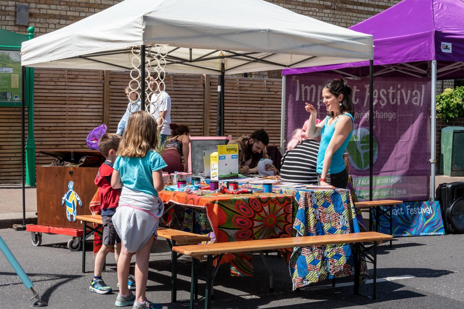 A woman talks to children next to colourful stalls and gazebos