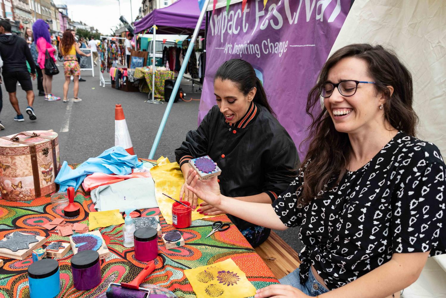 Two women take part in block printing at  a colourful table on the street