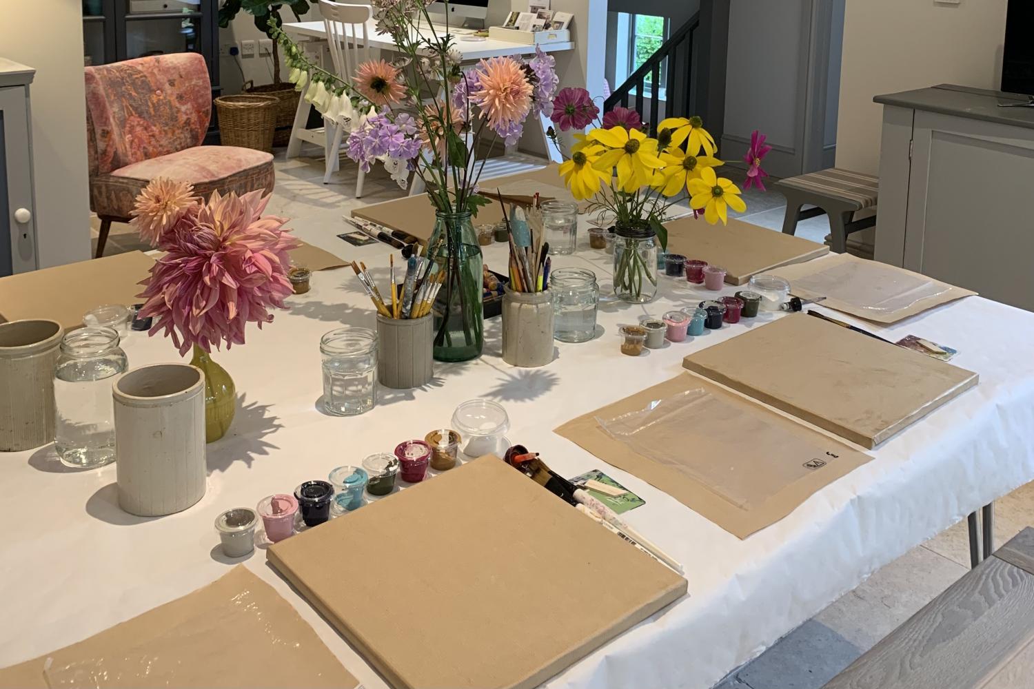 A table laid for an art class with paints, canvases and fresh flowers