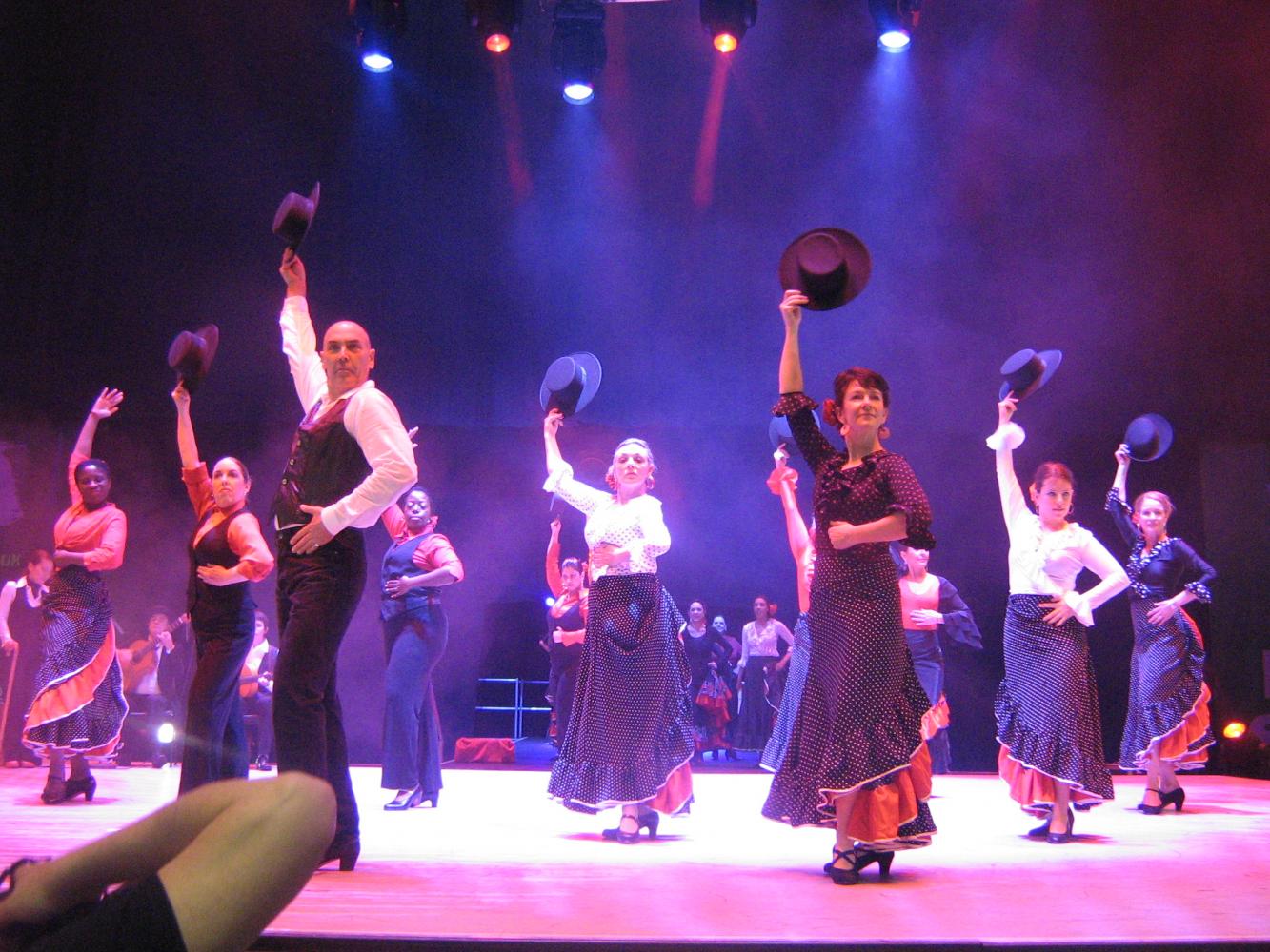 Large company of men and women dancing flamenco on dark theatre  stage