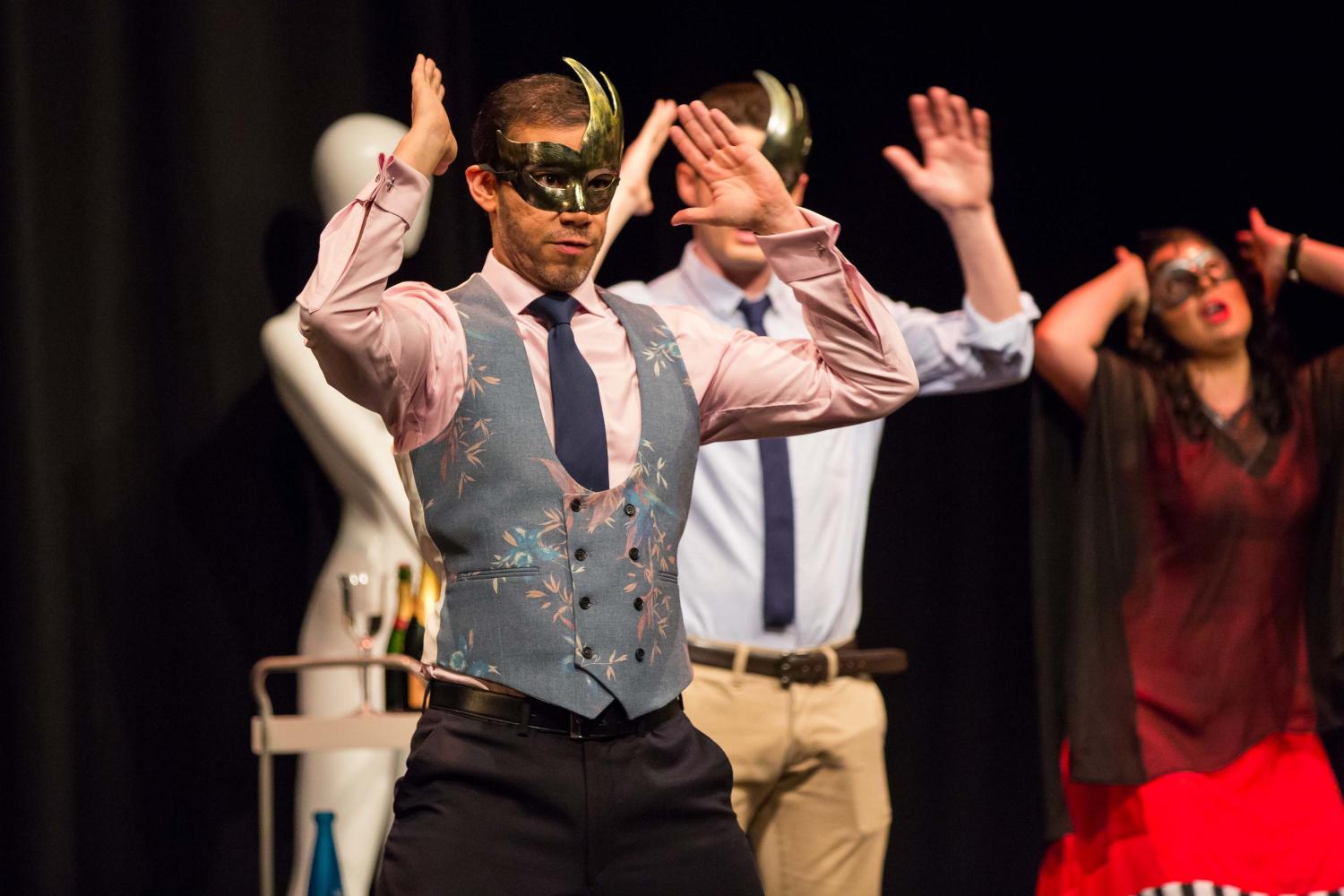 Three singers dancing in Vogue style in hold masks wearing smart trousers and waistcoats and dresses