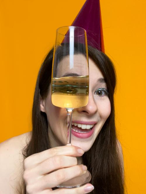 A colourful image of a young woman with a party hat on looking at us through a champagne glass. It's silly but fun.